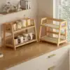 Two wooden countertop racks hold mugs, cups, and pitchers in a bright kitchen with sunlight streaming through blinds. | 28Alchemy