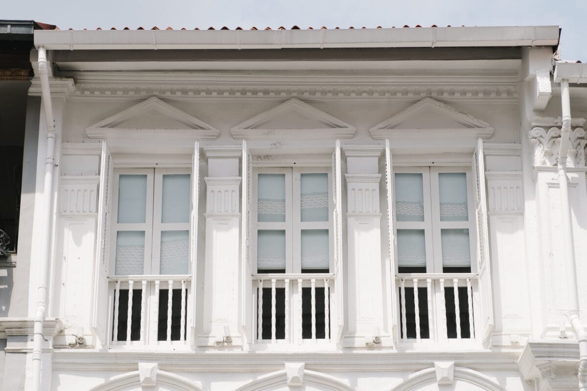 White colonial-style building facade with three large shuttered windows and decorative architectural details. | 28Alchemy