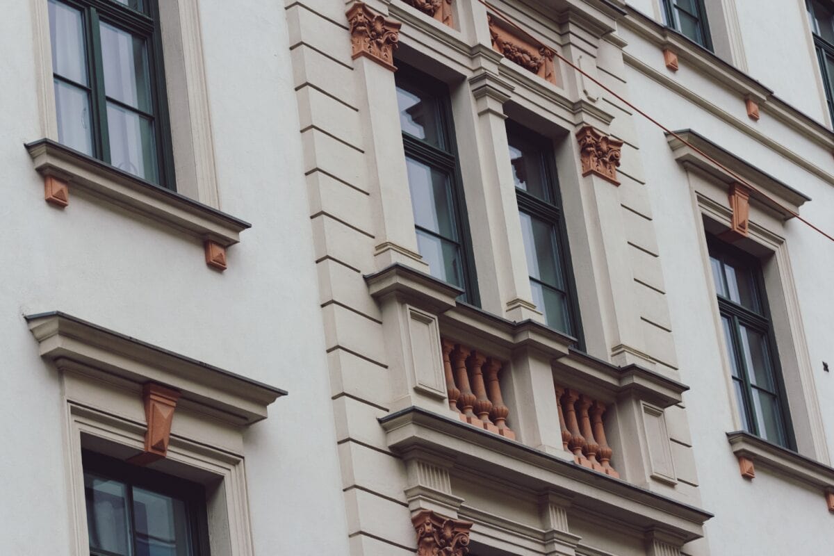 Ornate white building facade with tall windows, decorative trim, and small balcony featuring terracotta accents. | 28Alchemy