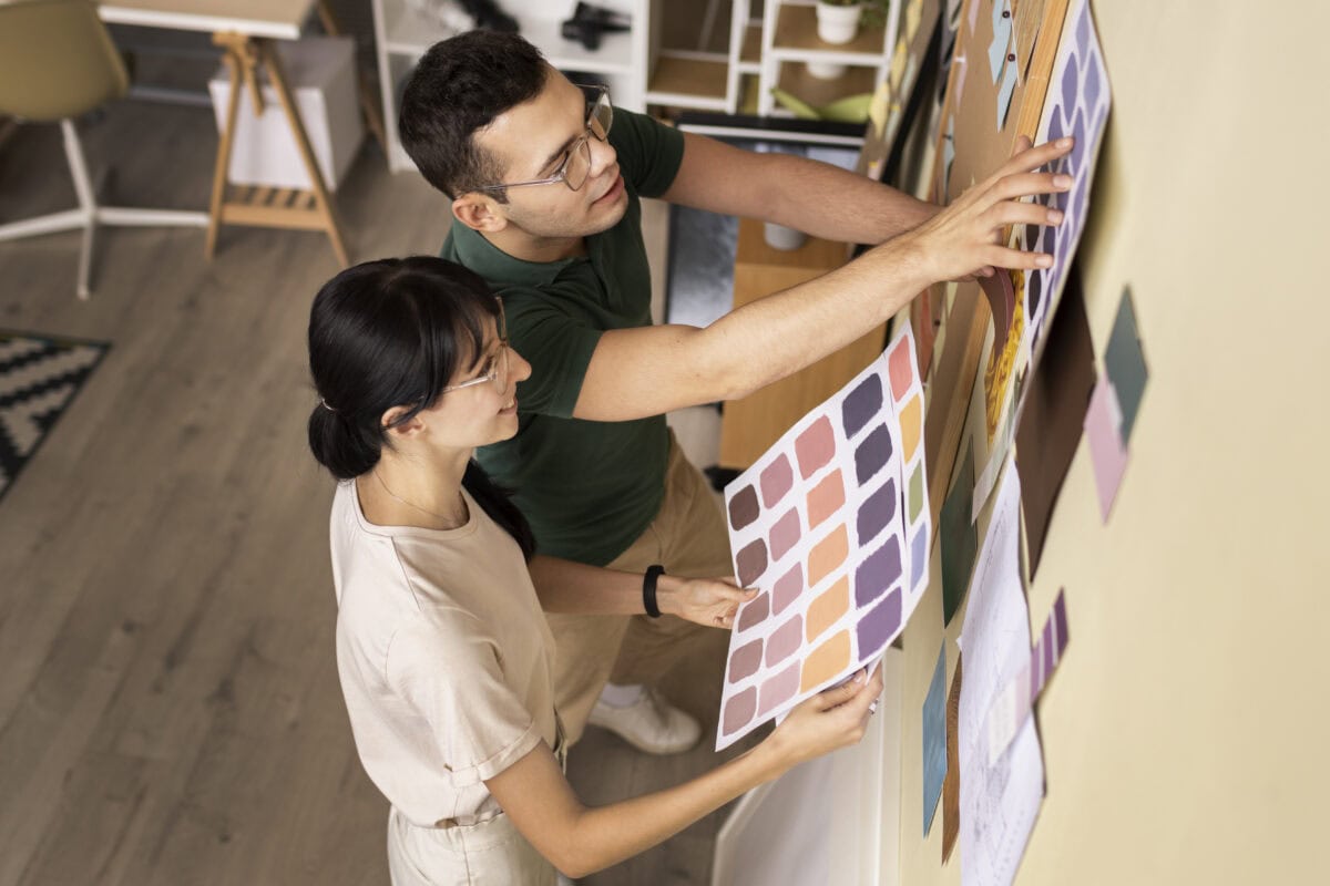 Two people examining color swatches on a wall, discussing and selecting colors in a creative workspace. | 28Alchemy