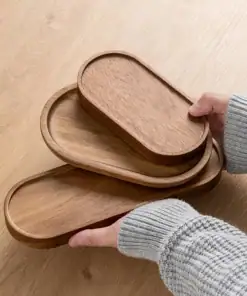 Hands holding three nested oval wooden trays on a light wood table. | 28Alchemy