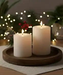 Two lit white pillar candles on a wooden tray, surrounded by festive greenery and string lights. | 28Alchemy