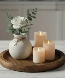 A white vase with flowers and three lit candles sit on a round wooden tray atop a light-colored table. | 28Alchemy