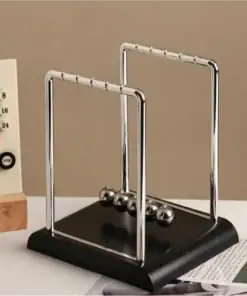 A Newton's cradle with metal balls sits on a desk near a calendar and a partially visible magazine. | 28Alchemy