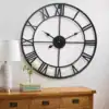 Large black wall clock with Roman numerals above a wooden dresser, next to a lamp, plant, and stack of books. | 28Alchemy