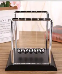 Newton's cradle with five silver balls on a black base, on a desk with books and a pink flower in the background. | 28Alchemy