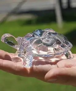 A person holds a small, clear glass turtle figurine in their hand outdoors, with grass in the background. | 28Alchemy