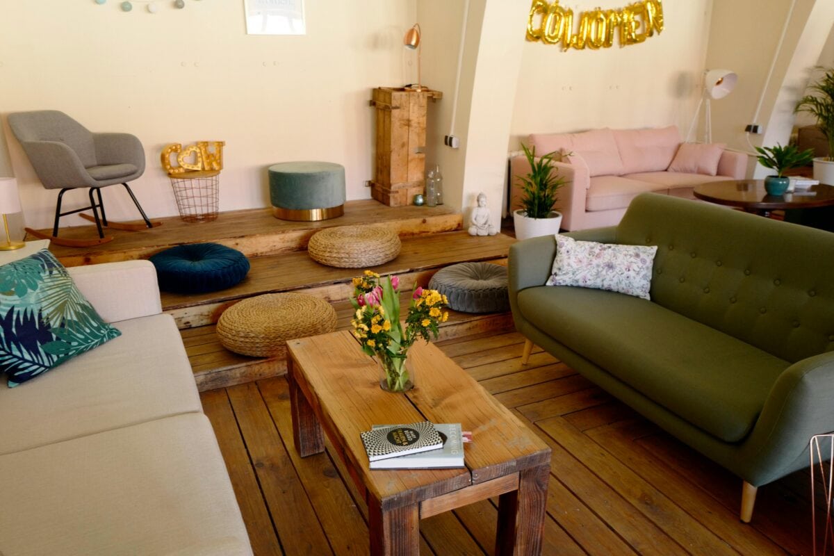 Cozy living room with couches, plants, a wooden coffee table with books and flowers, and decorative pillows and poufs. | 28Alchemy