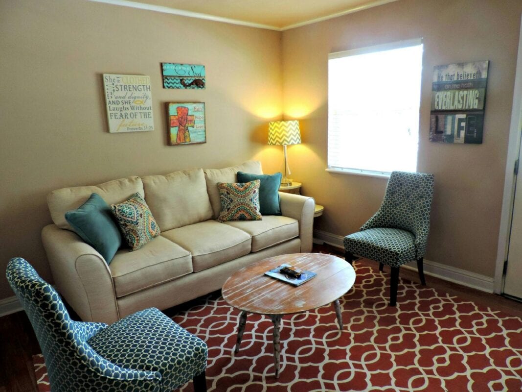 Cozy living room with beige sofa, blue chairs, patterned rug, wall art, and a small wooden coffee table. | 28Alchemy