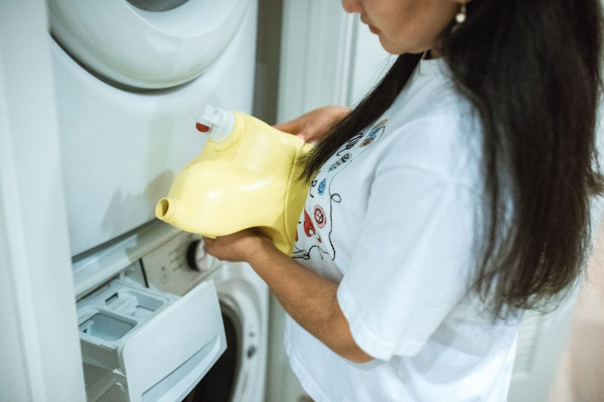 A person pouring detergent into a front-loading washing machine. | 28 Alchemy