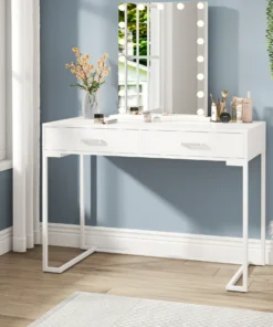 White vanity table with a mirror framed by lights, makeup items, and a vase with flowers against a blue wall. | 28Alchemy