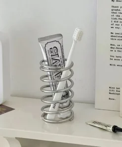 A toothbrush and toothpaste tube stand upright inside a spiral metal holder on a white shelf. | 28Alchemy