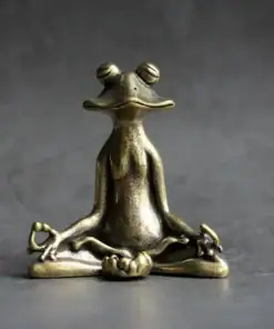 A bronze frog figurine sits in a meditative pose with crossed legs and closed eyes on a gray surface. | 28Alchemy