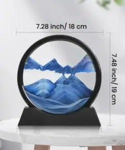 Round sand art frame with blue mountains, displayed on a black stand, with dimensions labeled 7.28 in by 7.48 in. | 28Alchemy