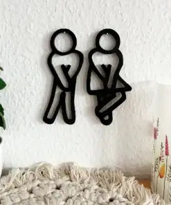 Black restroom symbols of a man and a woman with crossed legs, mounted on a white wall near plants and a candle. | 28Alchemy