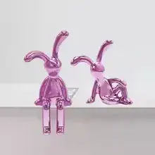 Two shiny pink rabbit figurines sit and recline on a white surface against a plain background. | 28Alchemy