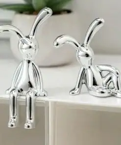 Two shiny silver rabbit figurines with long ears, posed playfully on a white surface with a plant in the background. | 28Alchemy