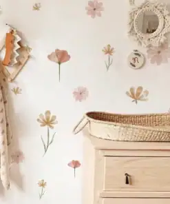 A nursery with floral wall decals, a woven basket on a wooden dresser, and hanging blankets on hooks. | 28Alchemy