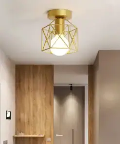 Modern ceiling light with a geometric gold frame and white bulb, installed in a hallway with wood and beige walls. | 28Alchemy