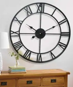 Large black wall clock with Roman numerals above a wooden dresser, next to a lamp, plant, and stack of books. | 28Alchemy
